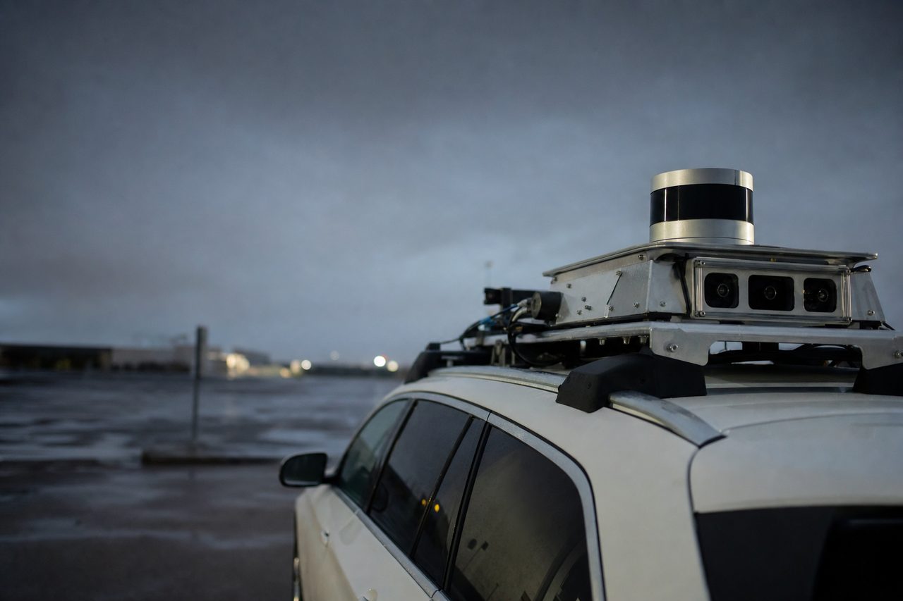 Roof-mounted lidar drum and camera cluster on an autonomous test vehicle at dusk