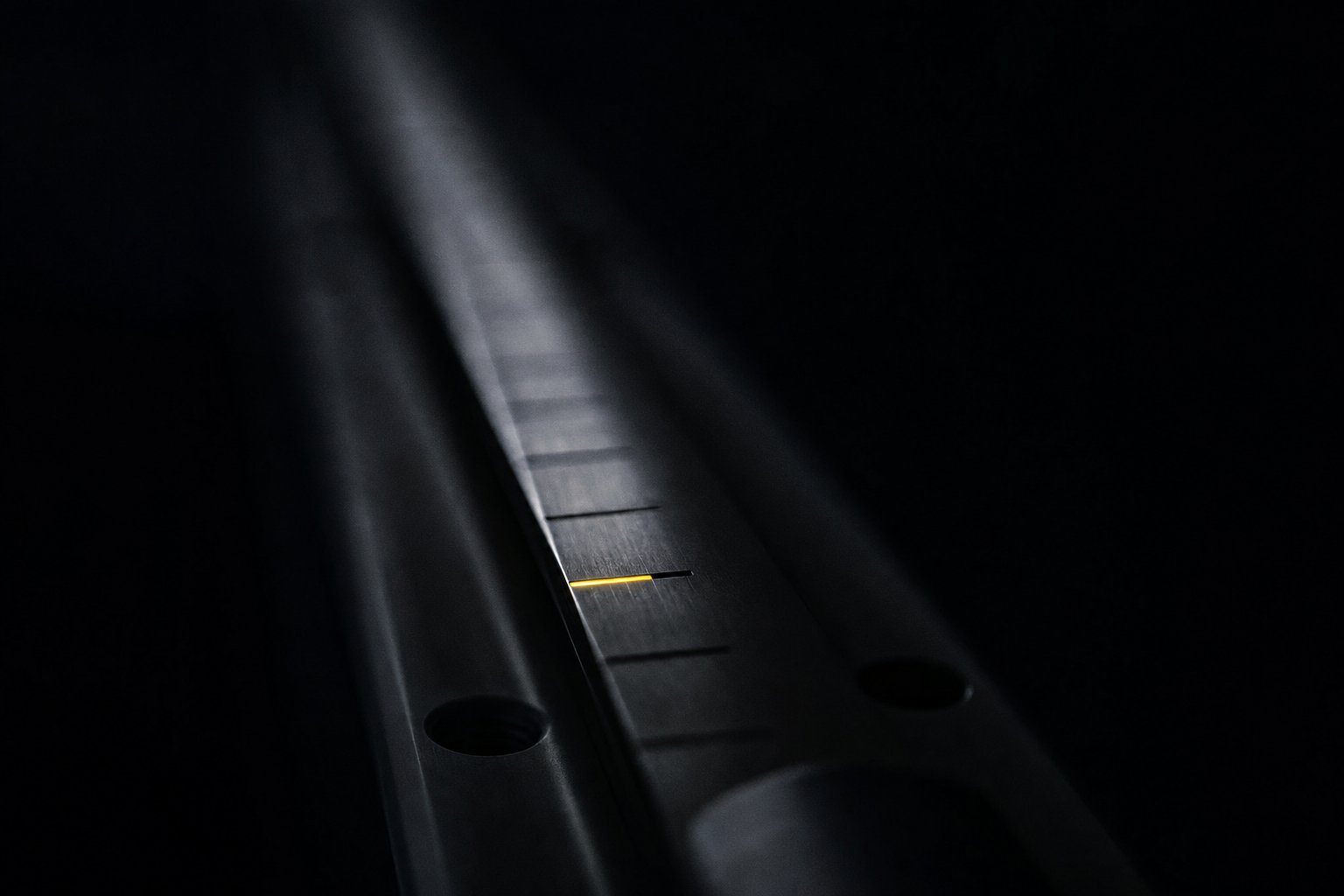 A dark machined rail marked with evenly spaced notches receding into shadow